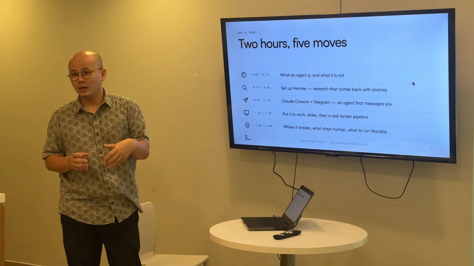 Haojun See teaching at the front of the room beside a screen showing the session's run of show, "Two hours, five moves"